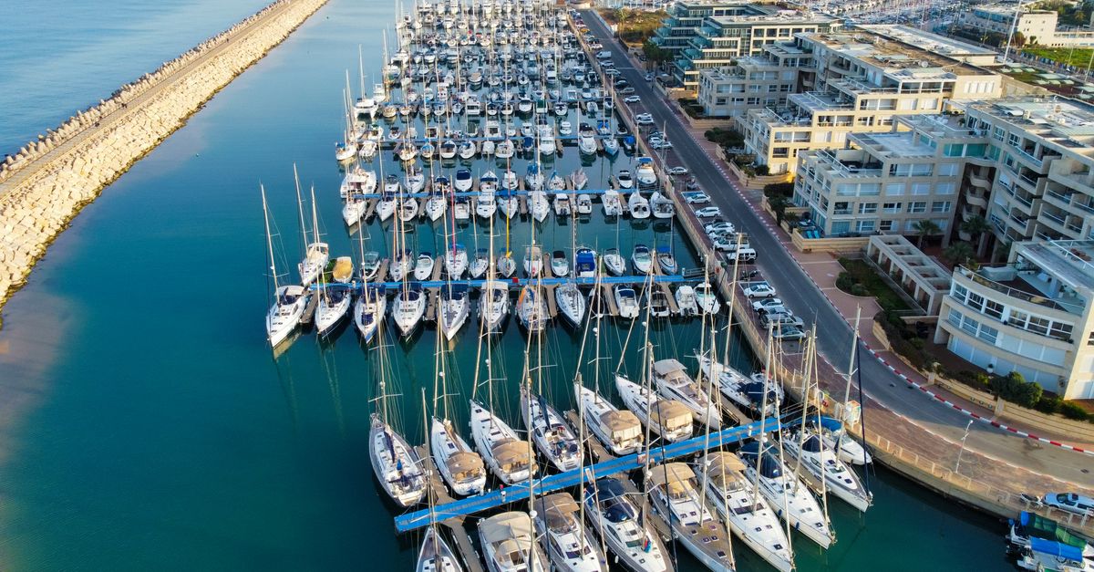 Aerial view of Herzliya Marina packed with docked sailboats on a sunny day in Israel.