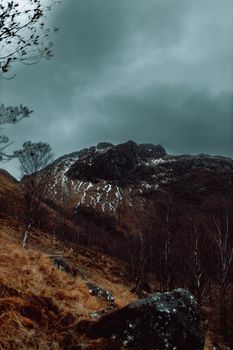 Moody mountain landscape with a dramatic cloudy sky and sparse vegetation in late autumn.
