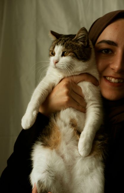 A smiling woman holds an adorable cat in a cozy indoor setting, capturing a moment of joy and companionship.