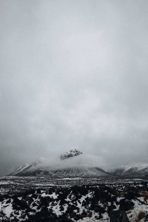 Free Gloomy winter landscape featuring a snow-covered mountain with foggy skies. Stock Photo