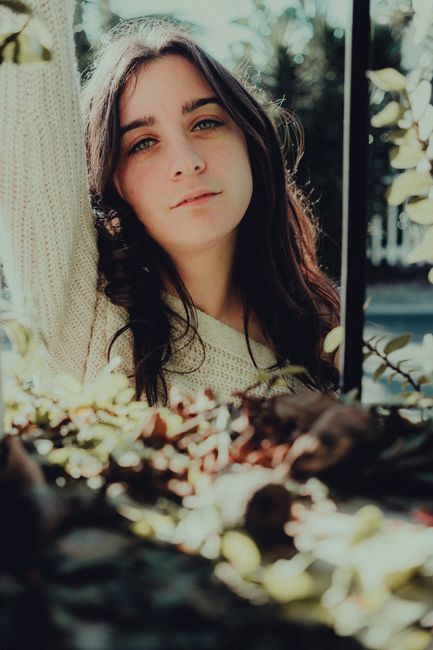 A natural portrait of a young woman outdoors, with sunlight highlighting her casual style.