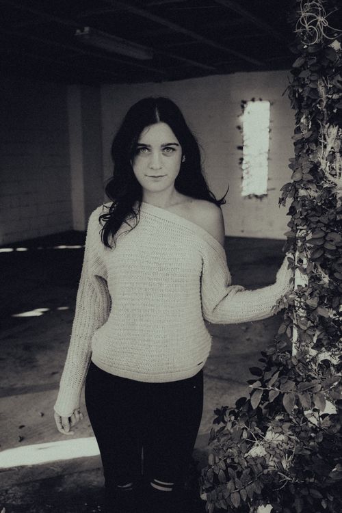 Free Young woman posing in a casual sweater indoors with a gritty urban atmosphere. Stock Photo