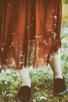 她脚穿黑色鞋子，身着飘逸的栗色裙子，置身于绿草如茵的户外环境中