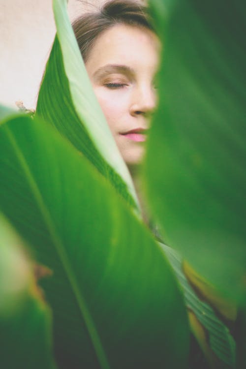 Free Woman Closing Her Eyes at the Back of Green Leaves Stock Photo