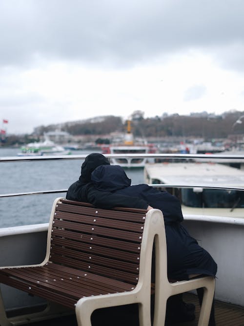 People in Jackets Sitting on Board on Sea Coast