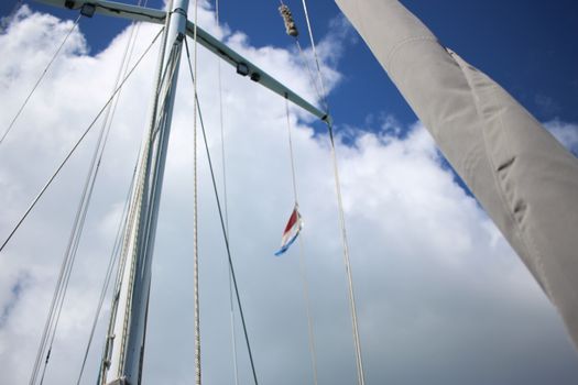 Low-angle view of a sailboat mast with ropes and a flag against a cloudy sky.
