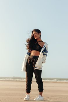 Young woman with flowing hair enjoys a sunny day on the beach, wearing casual fashion.