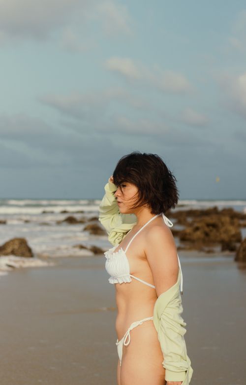 Free Side view of a woman in a white bikini on a sandy beach with rocky shoreline on a sunny day. Stock Photo