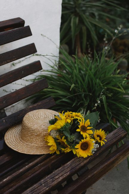 A straw hat and sunflower bouquet on a rustic wooden bench outdoors, evoking a summer vibe.