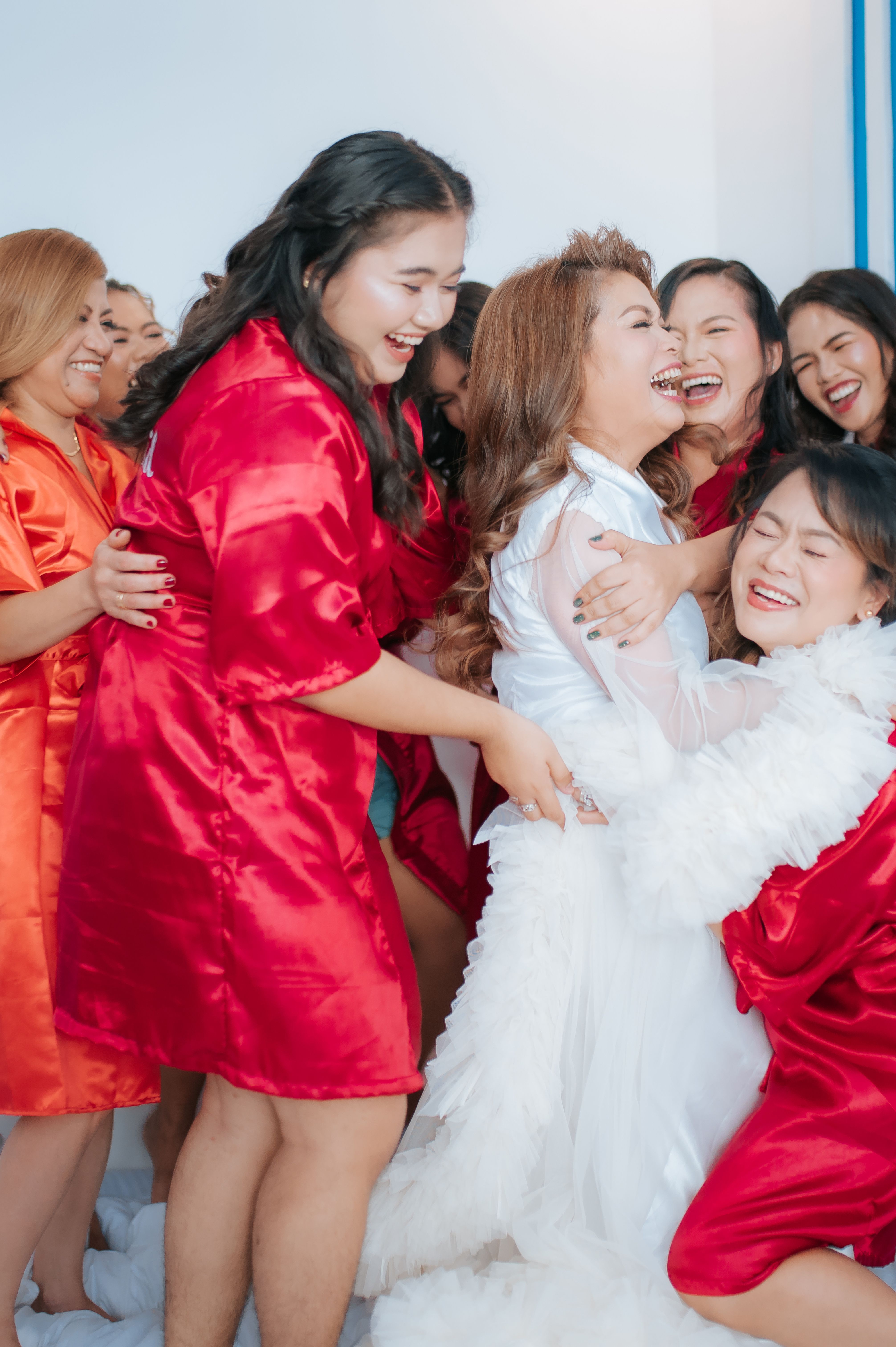 A joyful bridal party laughing and hugging while dressed in vibrant red robes indoors.