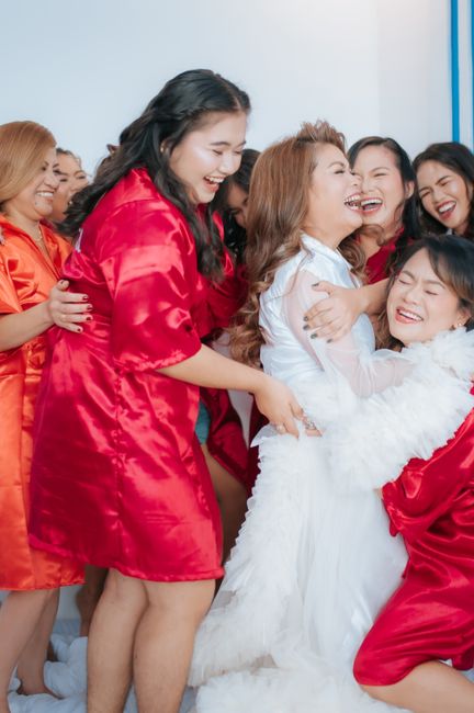A joyful bridal party laughing and hugging while dressed in vibrant red robes indoors.