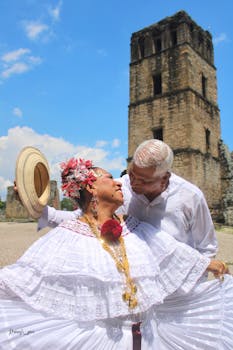Elderly couple embracing in traditional Panamanian attire in front of a historic tower in Panama City.