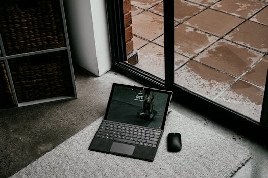 Elegant workspace setup featuring a laptop and mouse next to a window with a brick background.