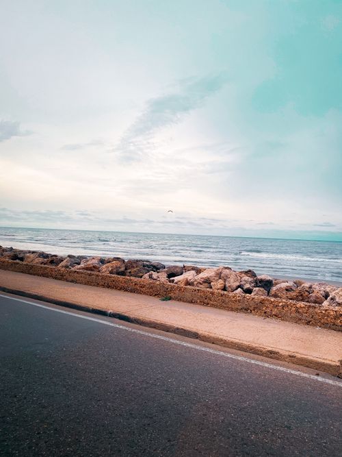 Free A tranquil scene of a coastal road beside a rocky shore under an overcast sky. Stock Photo
