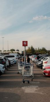 A bustling parking lot filled with cars and shopping carts under a clear sky.