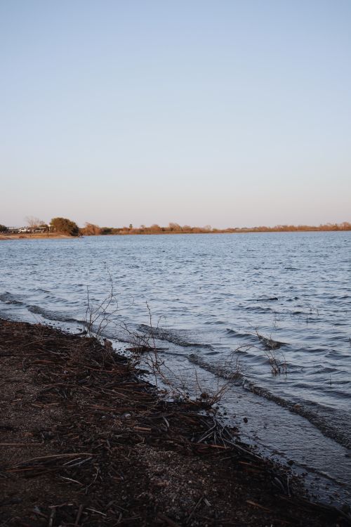 Free Peaceful lakeshore scene at sunset with calm waters and distant horizon. Stock Photo