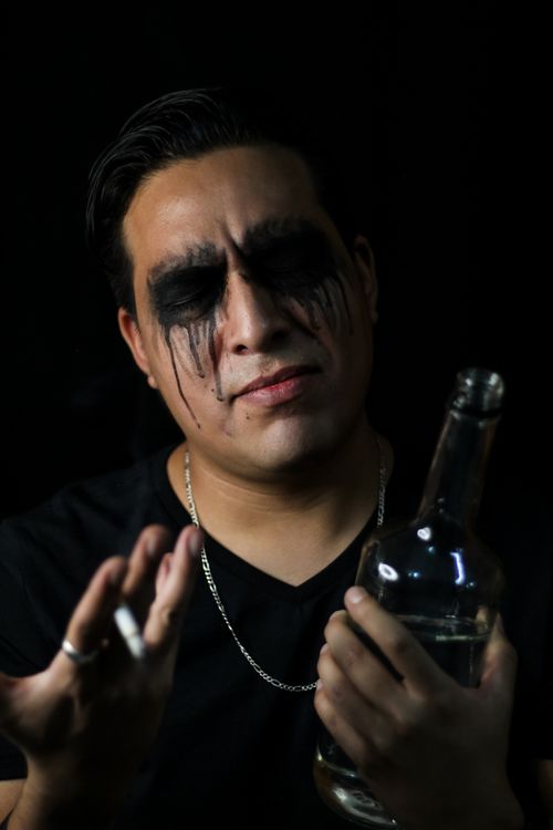 Free Intense portrait of a man with smeared makeup holding a bottle in low lighting. Stock Photo