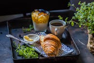 托盘上布置了美味的早餐，有羊角面包、咖啡和酸奶冻糕
