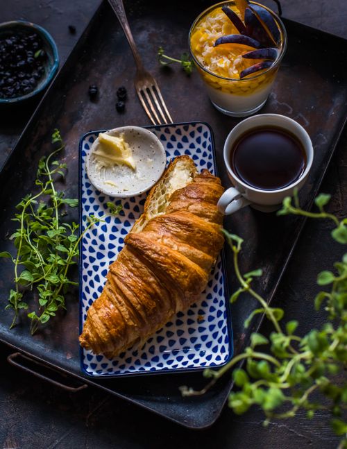 Free A delicious breakfast with a flaky croissant, butter, and coffee, served on a rustic tray. Stock Photo