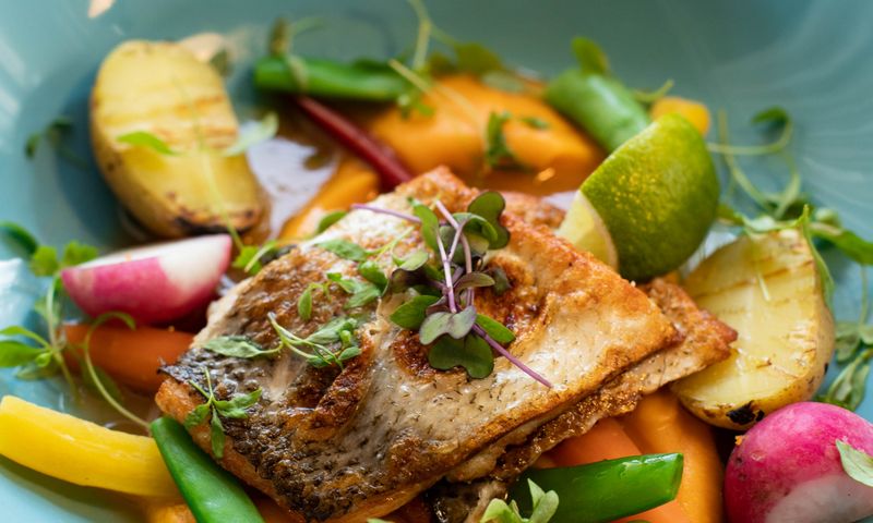 Filé de peixe grelhado com legumes em prato sobre mesa