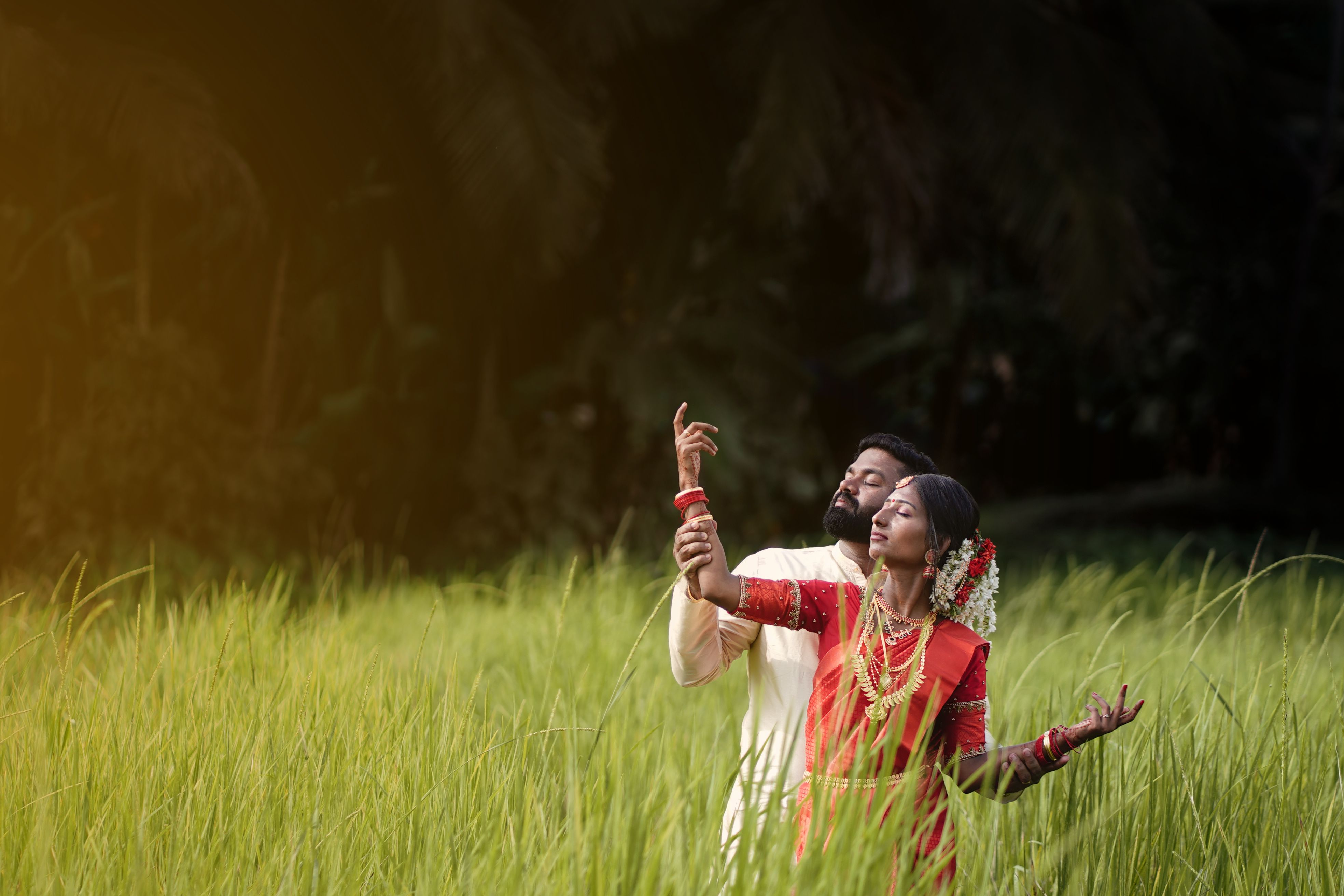 A couple in traditional Indian attire posing romantically in a vibrant green field in Kozhikode, India.