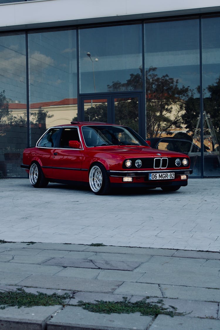 A Red BMW E30 Parked In Front Of A Building 