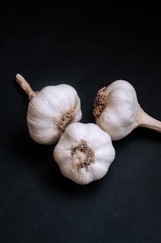Three fresh garlic bulbs on a black background in a minimalist food still life composition.