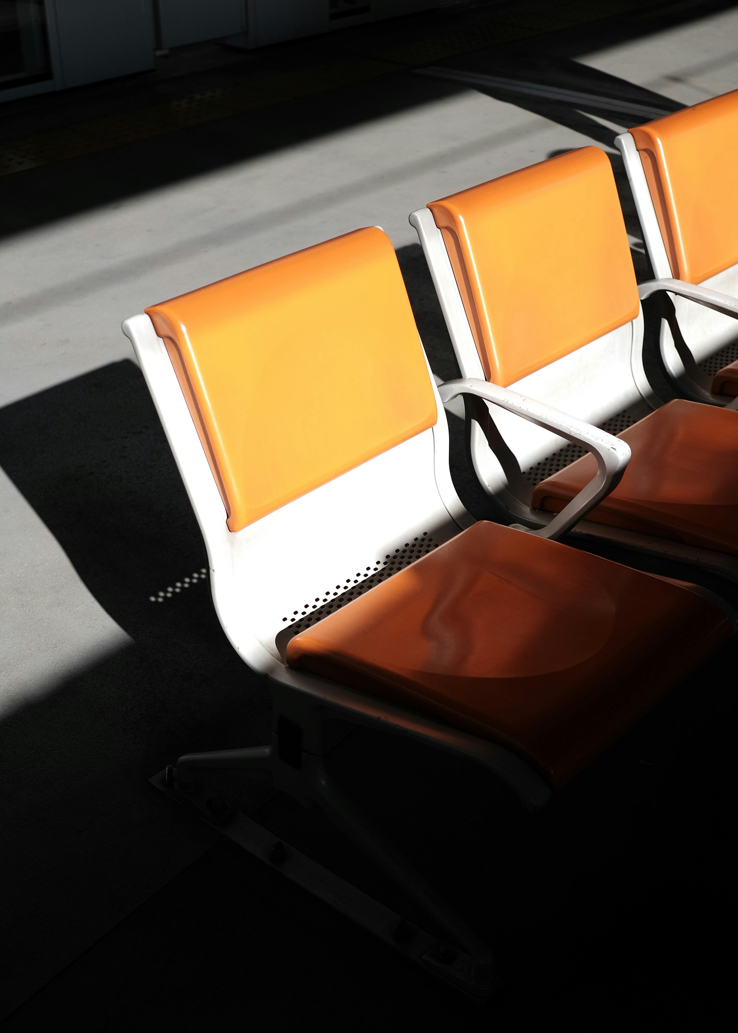 Orange chairs casting shadows in a Tokyo subway station, showcasing modern minimalist design.
