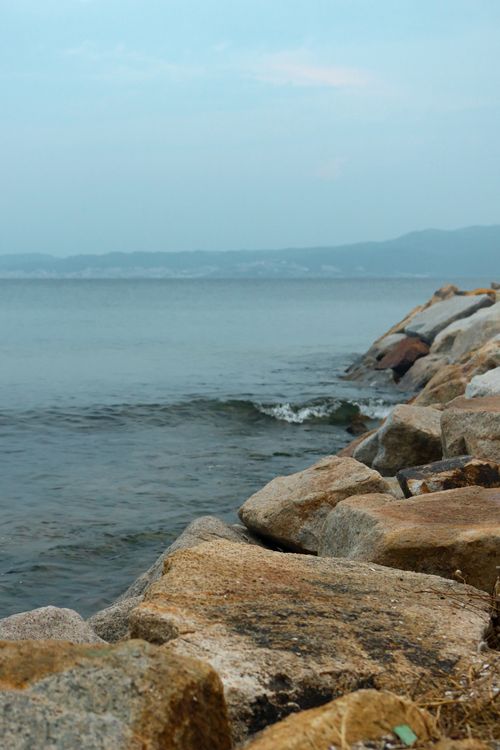 Free A serene seaside landscape featuring a rocky shoreline against a calm sea and blue sky, perfect for relaxation themes. Stock Photo