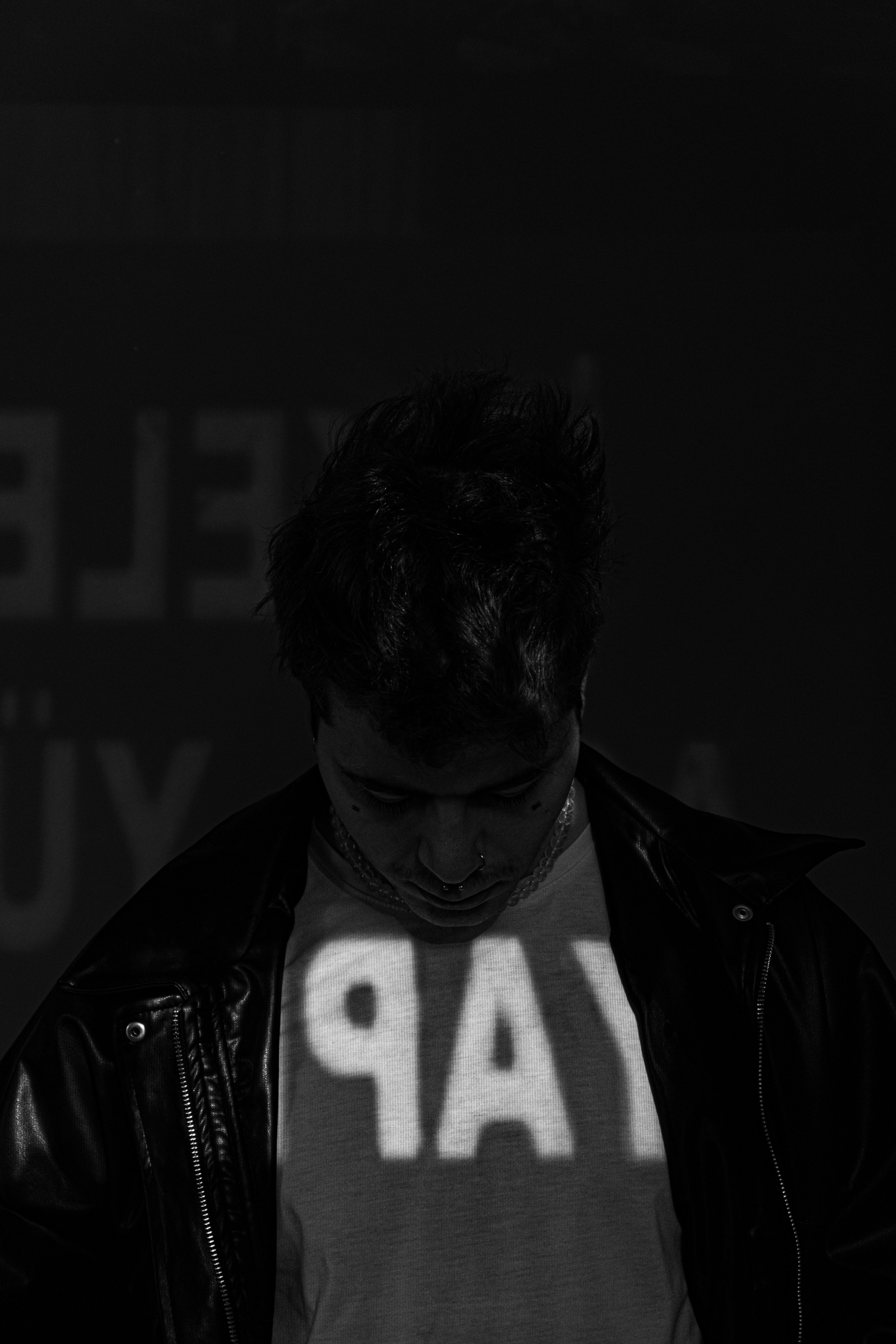 A mysterious black and white portrait featuring a person in a leather jacket with projected text shadows.