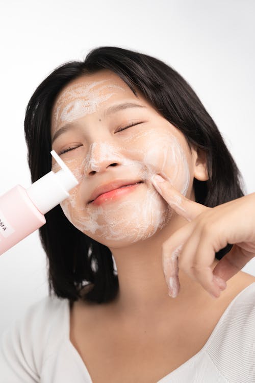 Young Smiling Woman with Facial Cleanser Applied to Her Face Holding a Bottle