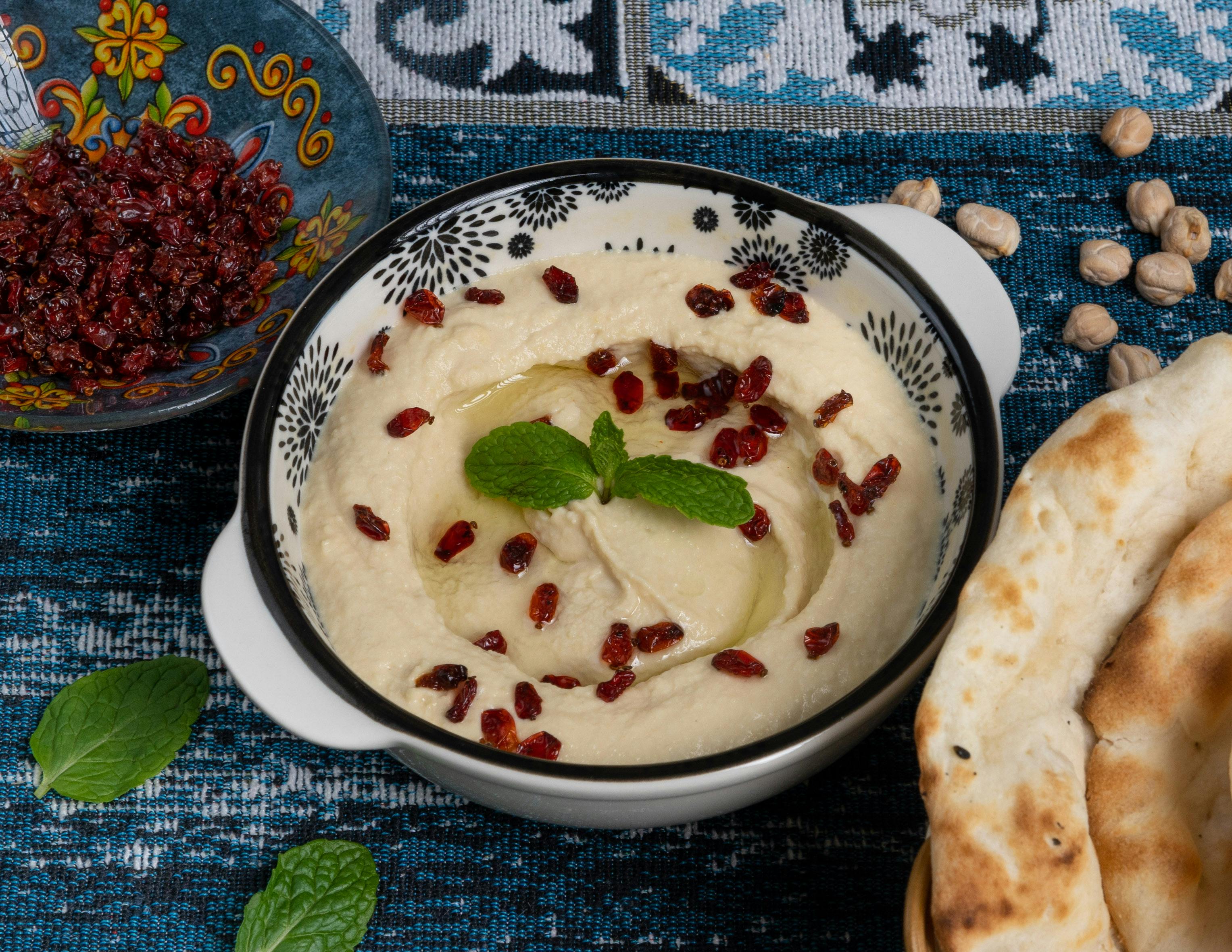 a bowl of hummus with pomegranate seeds and bread