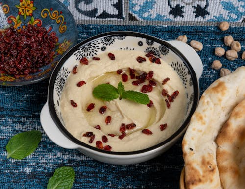 A bowl of hummus with pomegranate seeds and bread