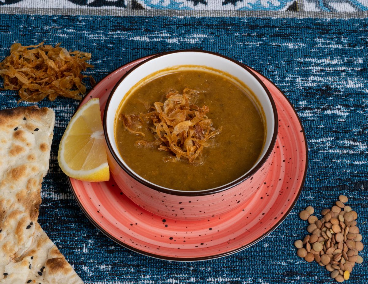 A bowl of thick haleem-style lentil porridge topped with fried onions and lemon