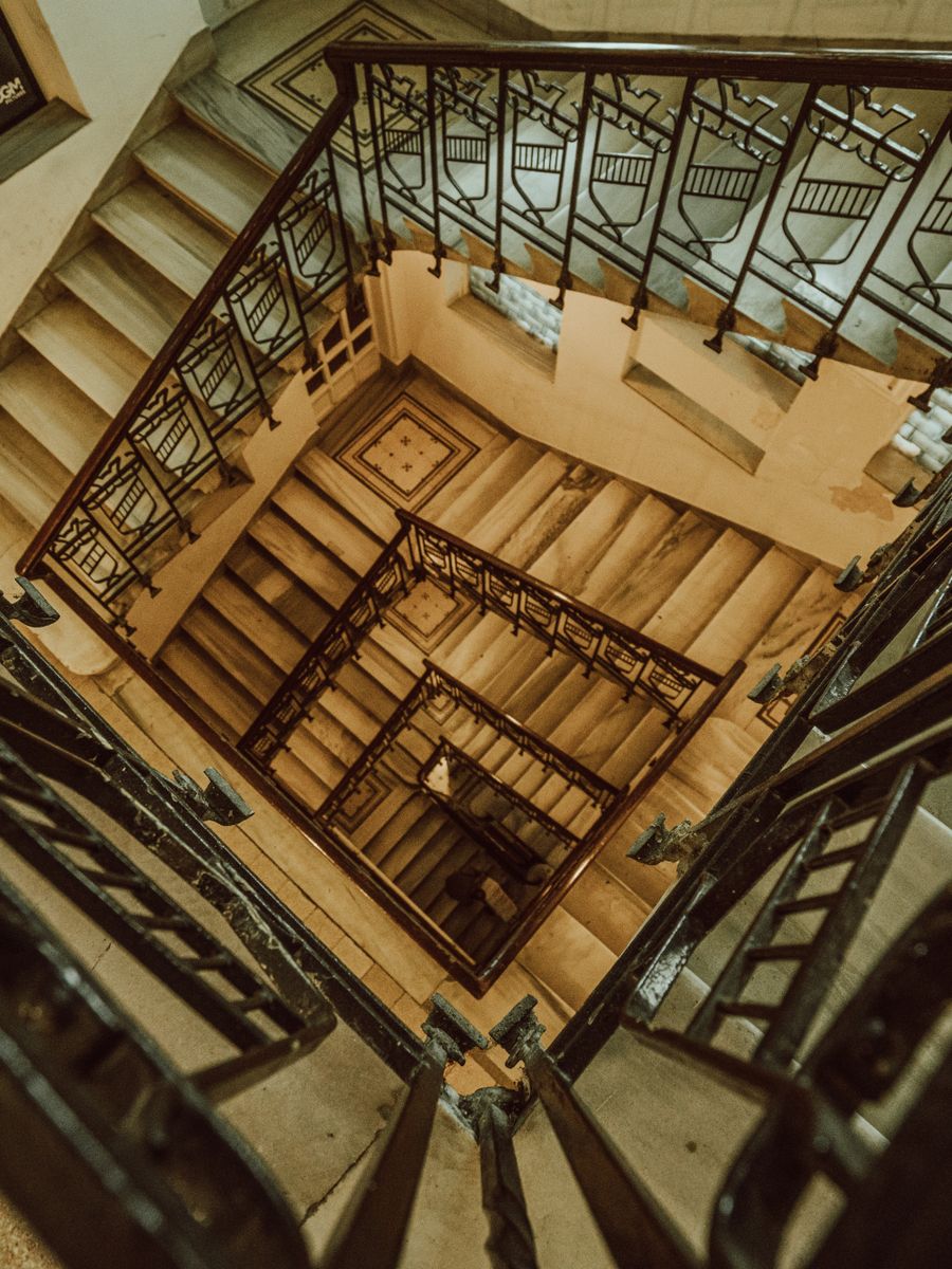 Vue en contre-plongée d'un escalier en colimaçon dans un immeuble ancien, avec sa rampe en ferronnerie.