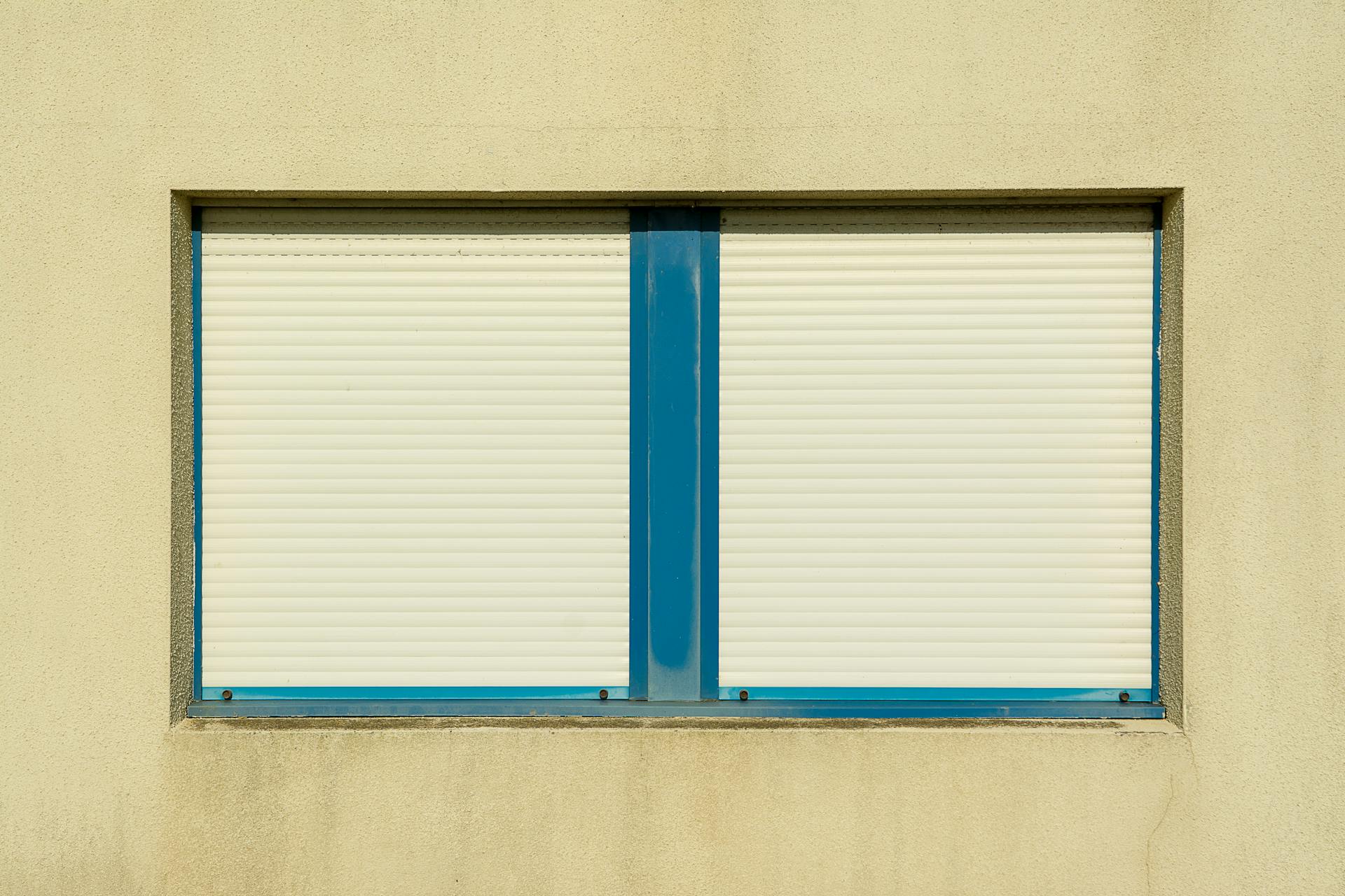 Close-up of a beige wall featuring blue framed closed window shutters, symbolizing safety and privacy.