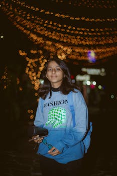 Portrait of a young woman in a trendy sweater under festive lights in Pokhara, Nepal at night.