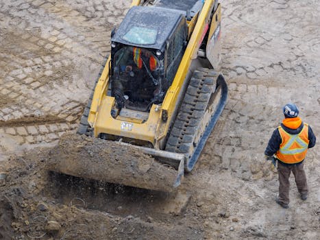 Top view of a bulldozer and worker on a construction site preparing the ground.