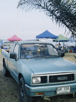 A classic blue Isuzu truck parked at an outdoor market with colorful tents in the background.
