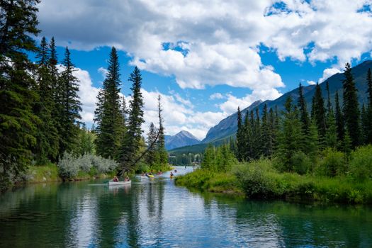 Enjoy a peaceful canoe ride on a river surrounded by lush forests and mountains under a cloudy sky.