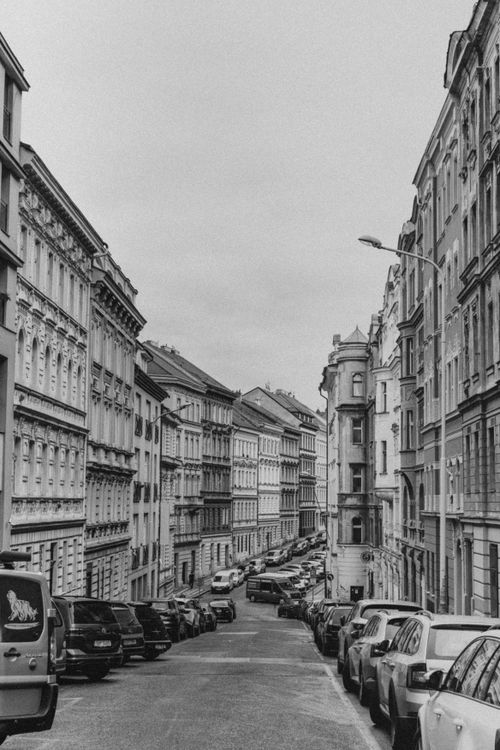 Free Black and white view of a European urban street lined with historic buildings and parked cars. Stock Photo