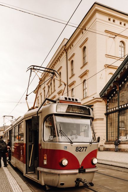 A vintage tram passes through a historic European street on a cloudy day.