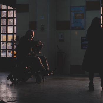 Silhouette of a person in a wheelchair inside a hospital corridor during sunset.