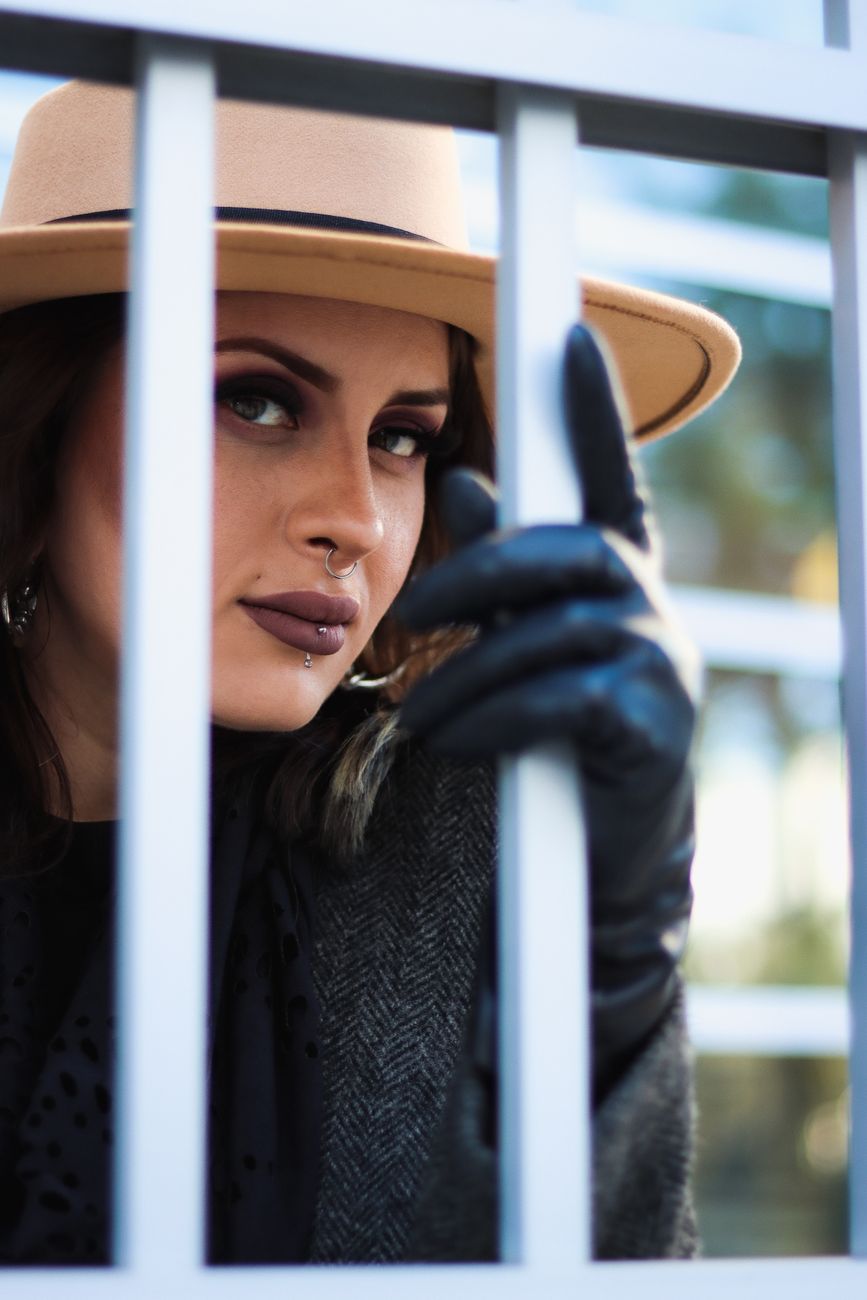 Mystique of a stylish woman in a hat looking through metal railing.