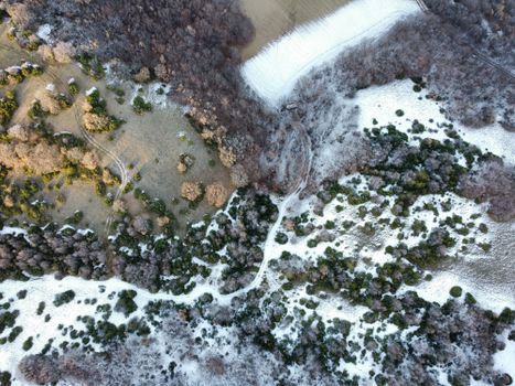 Drone view of snowy fields and forests, capturing winter's serene beauty.