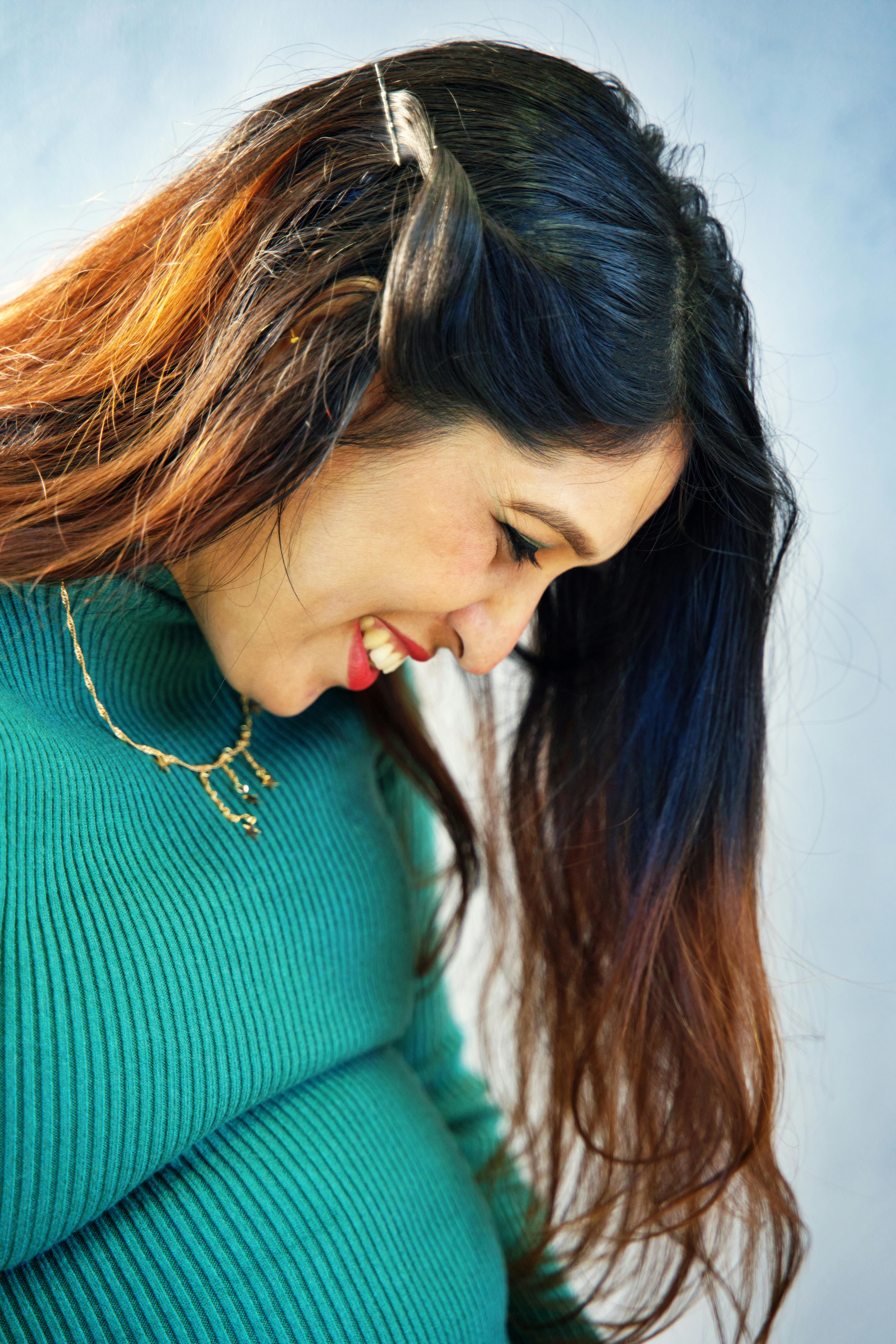 Side profile of a smiling pregnant woman in a green sweater with jewelry.