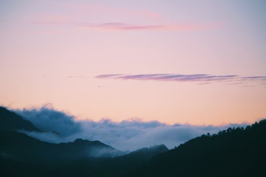 Serene view of misty mountains and pink clouds at sunset, capturing nature's tranquil beauty.
