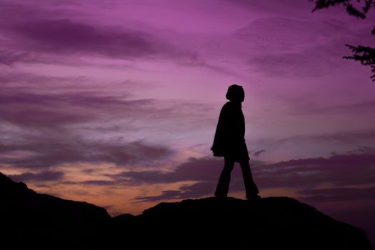 A woman stands silhouetted against a stunning purple and orange sunset sky, evoking a sense of tranquility.