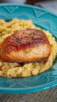 Close-up of perfectly grilled salmon served on a bed of creamy risotto in a blue dish.