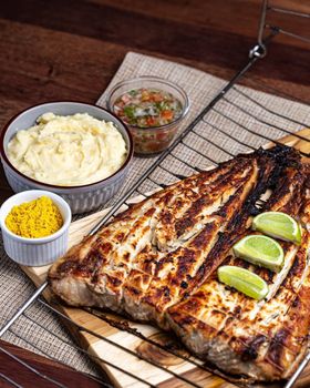 Delicious grilled fish served with lime, mashed potatoes, curry powder, and salsa on a wooden board.